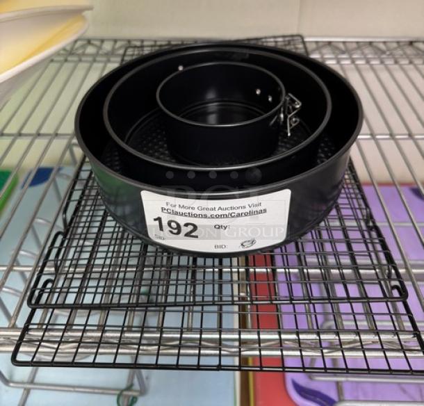 Expandable cake pans set with 4", 7", 8.5" sizes and cooling racks, in good condition, auction tag number 192 visible.