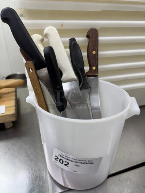 Assorted knives and spreaders in a white container, featuring wood and plastic handles, varying blade designs. Lot 202 label.