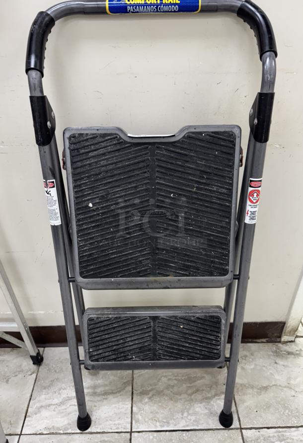Werner two-step stool with black anti-slip treads, foldable handle, and gray metal frame. Visible safety labels, used condition.