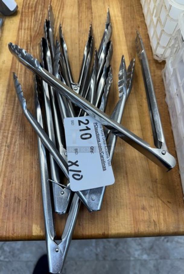 Set of 10 metal tongs on a wooden surface, each with scalloped edges. Auction tag reads "210 x10 Qty." Ideal for kitchen use.