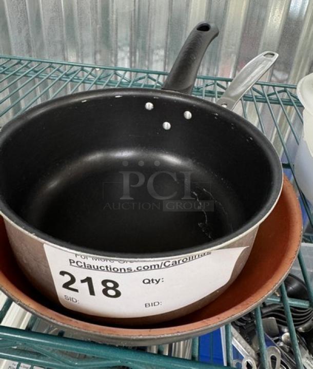 Two pans: a black sauce pan with handle and a brown small frying pan underneath; small surface wear visible; auction label 218.