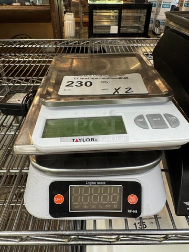 Taylor Digital Scales, model KF-H8, shown on metal shelf. Clear display, stainless steel platform, good condition.