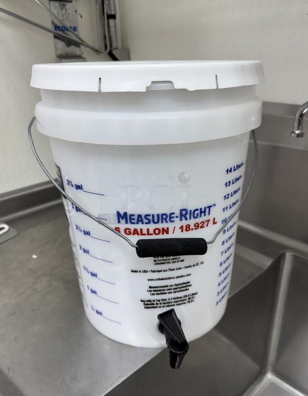 Measure-Right 5 Gal. mixing container with lid, marked with volume graduations in gallons and liters, includes spout and metal handle.