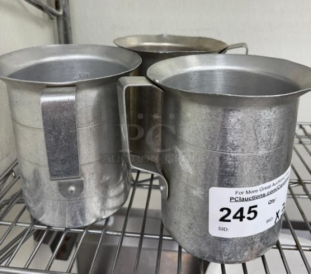 Three metal 2 Qt. measuring cups on a shelf, each with a sturdy handle. Visible auction label with lot number 245.