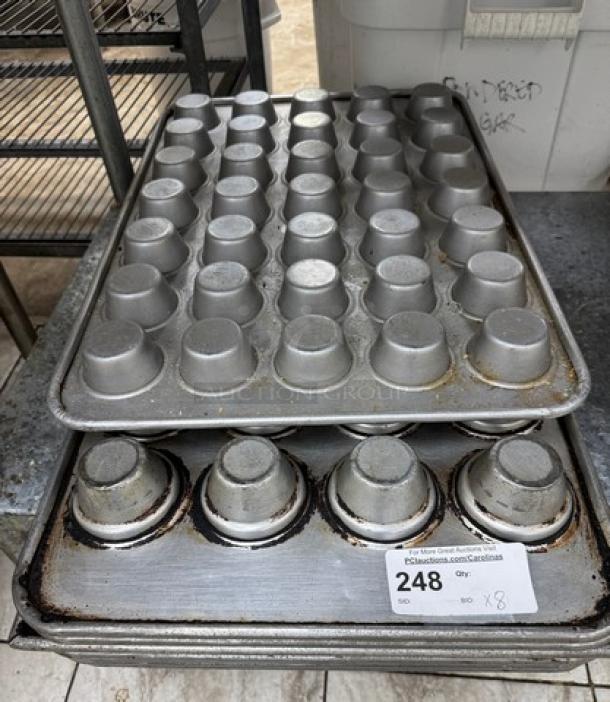 Set of eight metal cupcake pans, used condition, stacked with visible wear and auction tag indicating lot number 248.