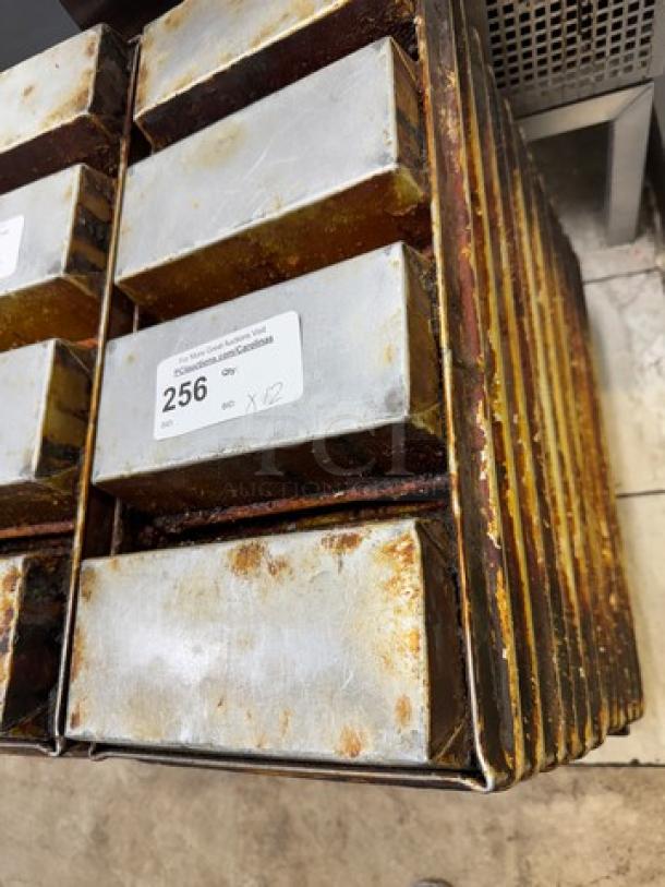Twelve used metal bread pans stacked vertically, showing signs of wear. Auction label reads "256, Qty 12."