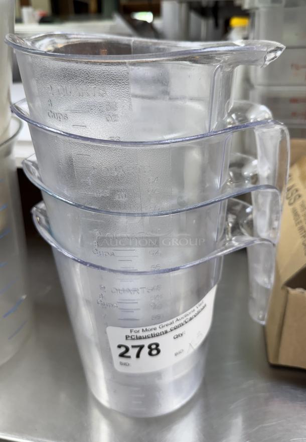 Stack of clear 2-cup measuring cups with visible volume markings and auction label. Set of four in used condition.