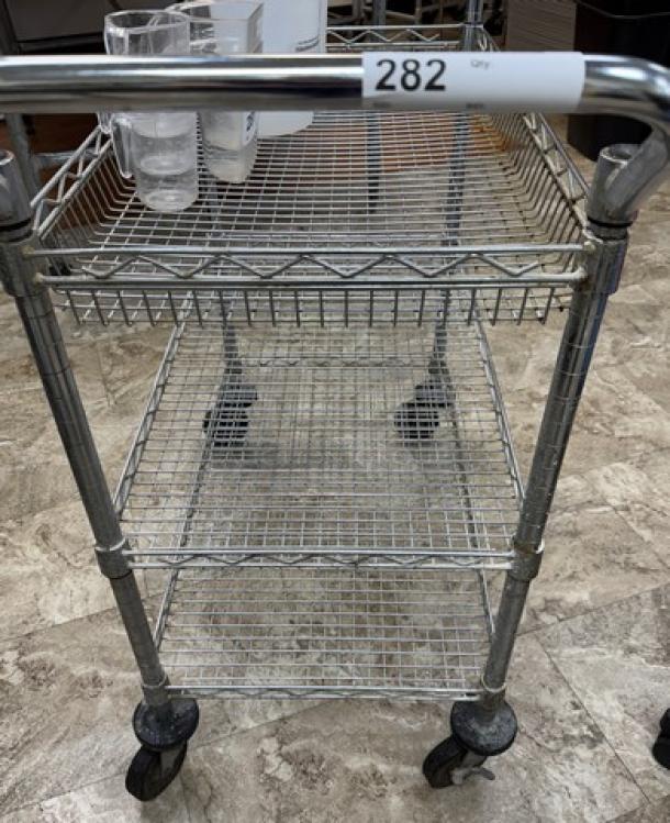 Rolling wire cart with 3 shelves, metal construction, casters for mobility, minor wear. Label marked "282."
