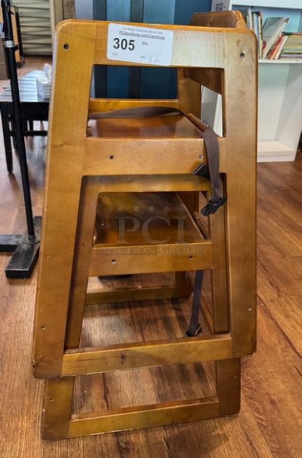Two wooden high chairs in sturdy condition, featuring safety straps. Auction tag "305" attached on the backrest.
