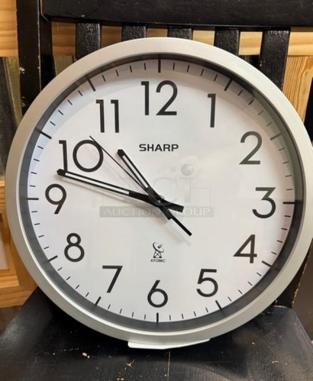 Sharp wall clock in silver frame, white face, black numerals, and hands. Marked "Sharp" and "Atomic" at center. Tested and working.