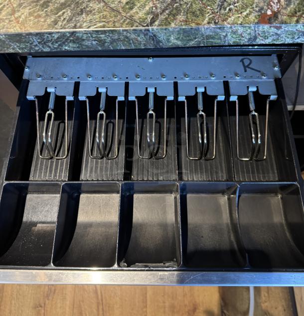 POS cash drawer with black compartments, steel clips, includes extra ribbon and paper, letter "R" marked inside.