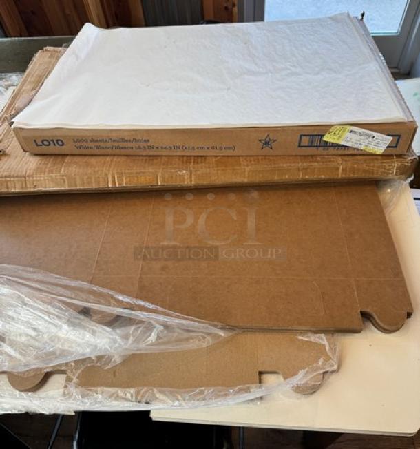 Assorted bakery supplies including parchment paper sheets, unassembled brown cardboard boxes, and plastic bags.