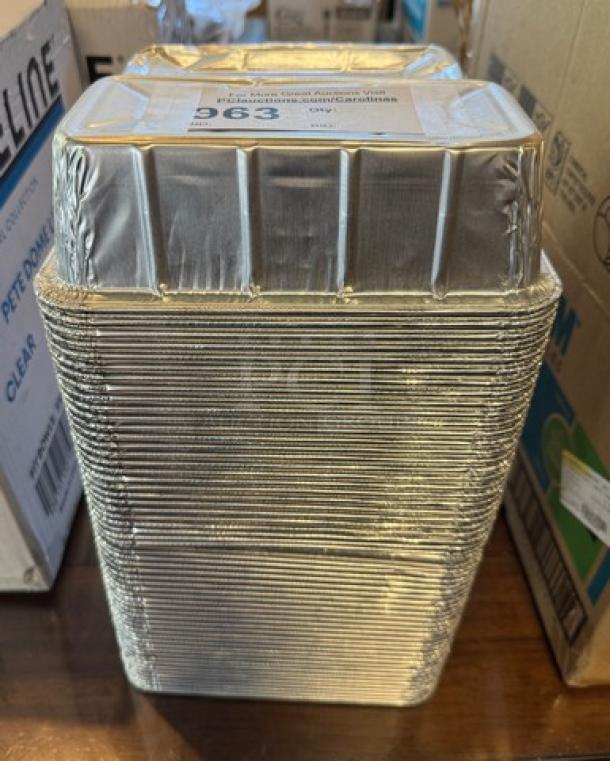Stack of disposable tin loaf pans, unused. Silver color with fluted sides. Sticker on top indicates item number 963.