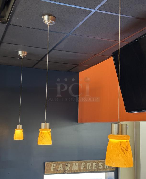 Three orange glass pendant lights, each 4.5" x 7", with silver fixtures, hanging from a dark ceiling.