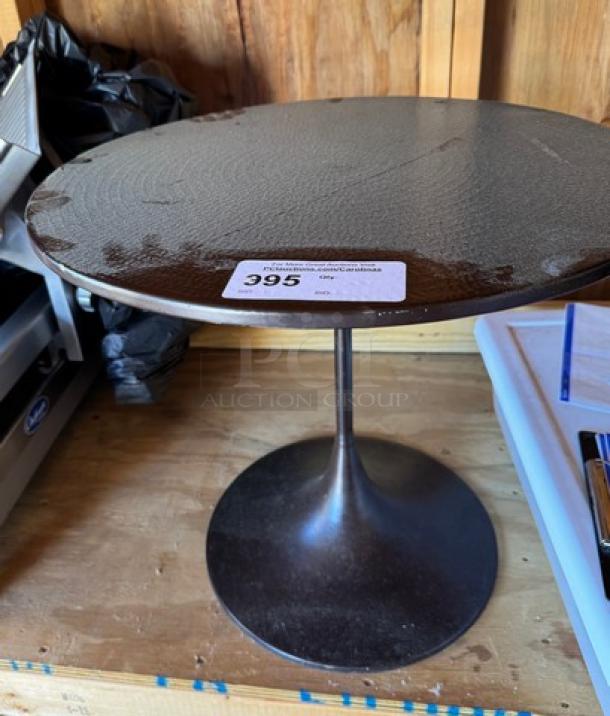 Round metal table with a textured, dark finish and single pedestal base. Auction label with number 395 on tabletop.