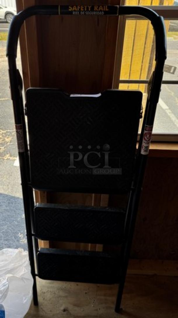 Foldable Safety Rail step stool ladder, black metal, three non-slip steps, used condition, safety labels visible.