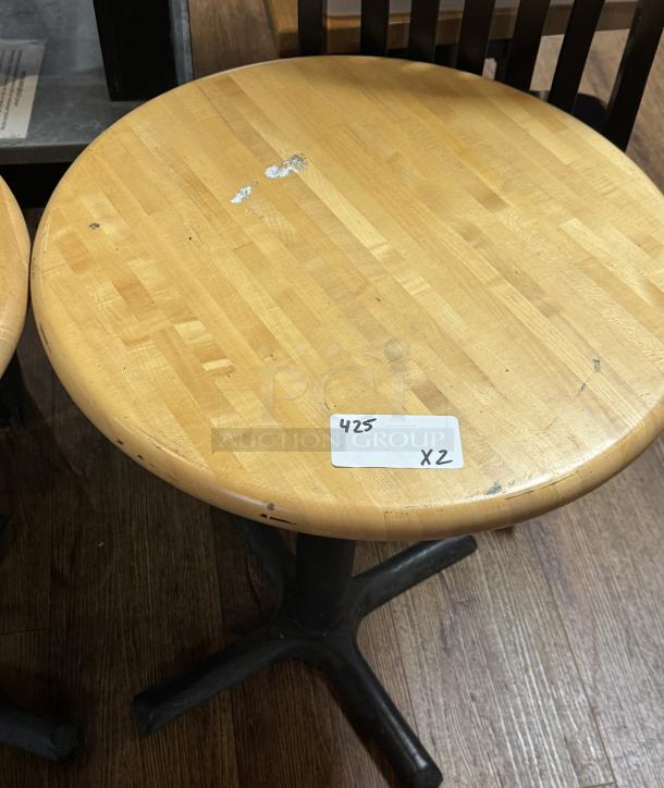 Round wooden dining table with light finish, some surface wear. Black metal pedestal base. Label indicates "425" and "x2".