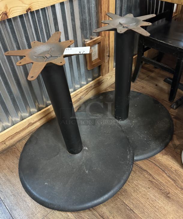 Two black metal table bases with star-shaped mounting tops, showing signs of wear. Tag reads "423 X2".