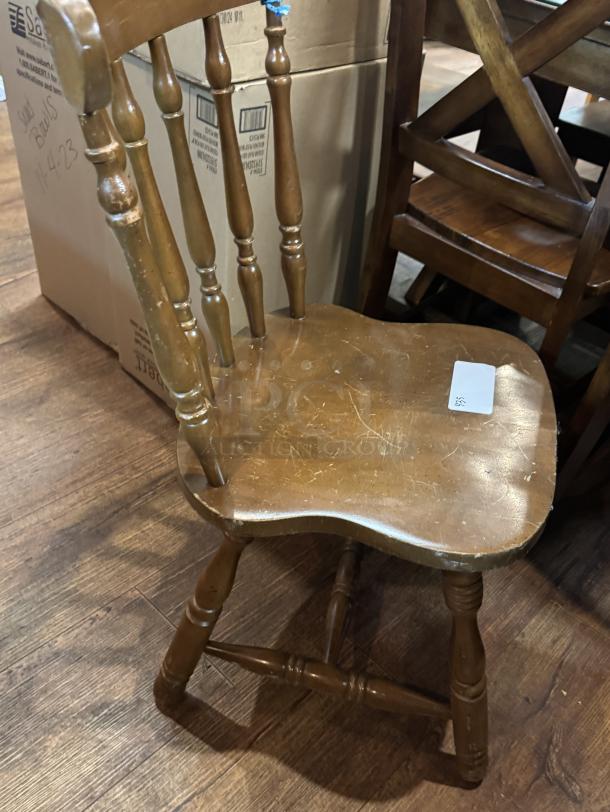 Wooden dining chair with spindle design, visible scratches, and a worn finish. Marking on seat indicates item number.