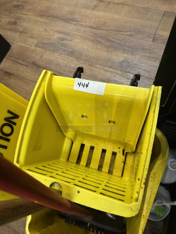 Yellow mop bucket with squeegee feature, labeled "444," in used condition on wooden floor.