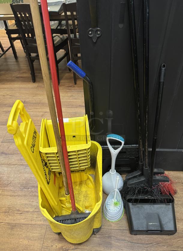 Yellow mop bucket with caution sign, broom, mop, dustpan set, and toilet brush. Used condition, suitable for cleaning tasks.