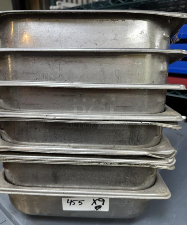 Stack of nine stainless steel half pans, showing scratches and wear. Label reads "455 x9." Suitable for catering.