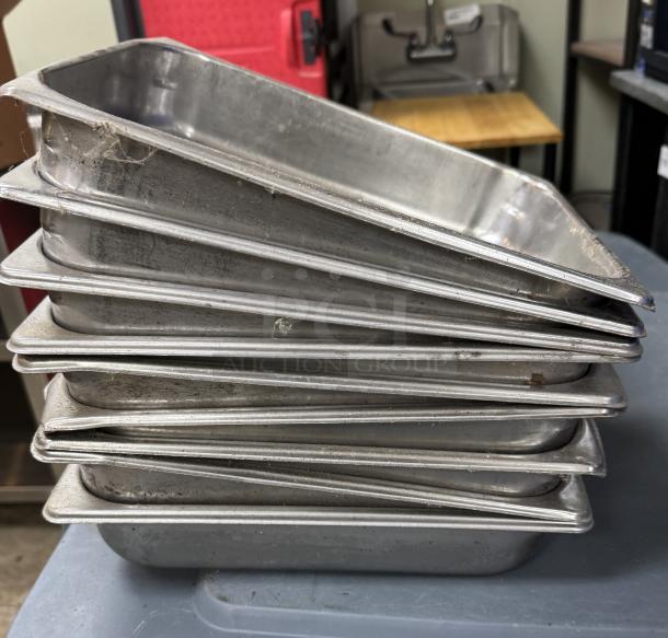 Stainless steel half pans, stack of 9, used condition, slight wear visible. Ideal for catering or kitchen use.