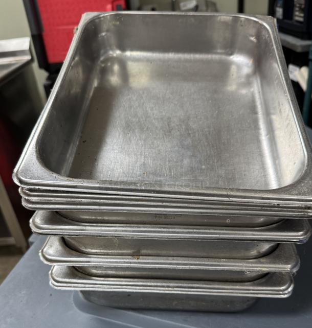 Stainless steel half-size pans, 9 pieces stacked. Used condition with visible markings. Size P/N 20229 engraved.