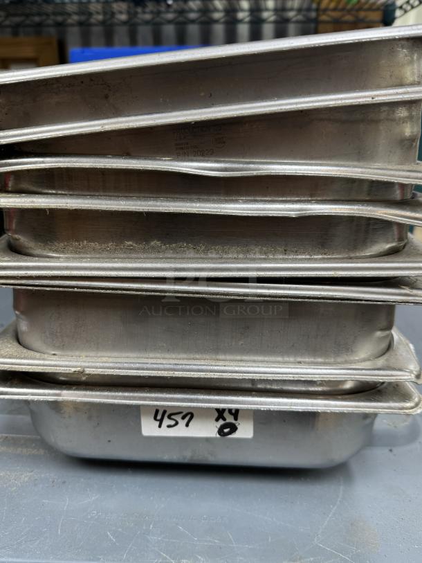 Stack of stainless steel half pans, 9 total, labeled "457 x 4," showing signs of use, ideal for catering or food service.