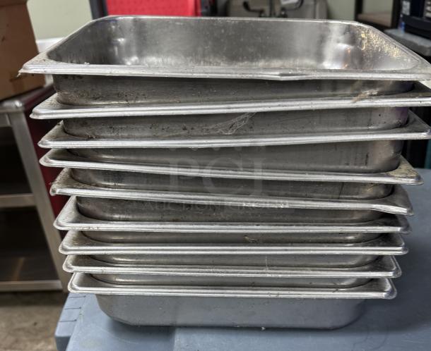 Nine stainless steel half pans stacked, showing signs of use, dimensions 12"x10", suitable for kitchen or catering.