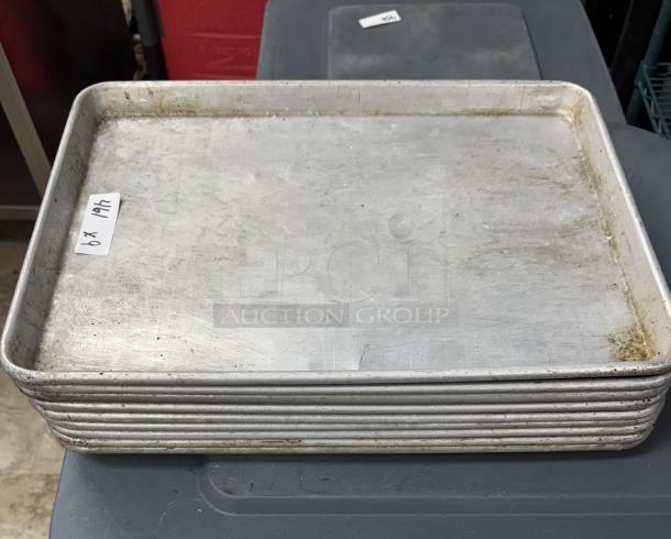 Stainless half-size sheet pans, stack of 9, used condition, visible wear. Dimensions: approx. 18x13 inches. Tag labeled "9 x".