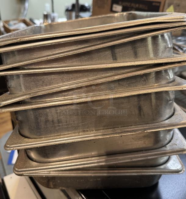 Stack of stainless steel half-size sheet pans, used condition, 9 pieces, showing surface wear and scratches.