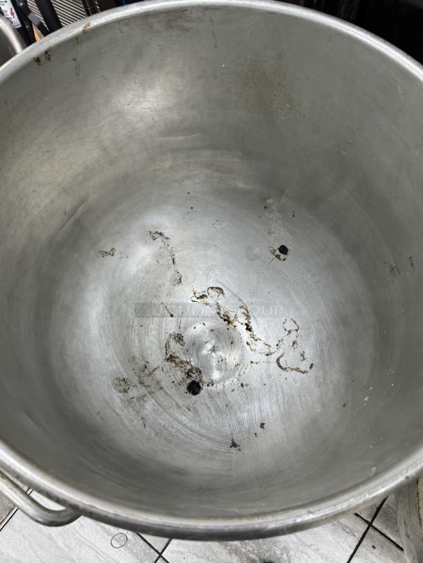 Steel 128 Qt. mixing bowl with visible wear and large capacity, equipped with sturdy handles, resting on a dollie.