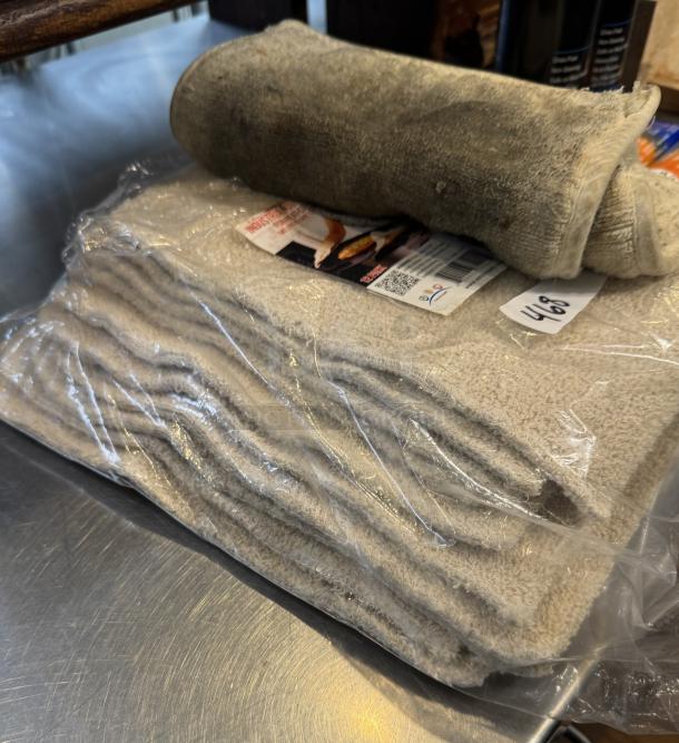 Industrial hot oven pads, 1-12 pack, packaged and placed on a metal surface, showing a durable beige material. Tags indicate product details.