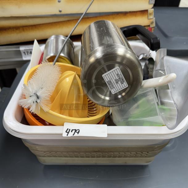 Assorted kitchen utensils with two collapsible dish racks; includes a brush, juicer, mug, and other items in a plastic bin.