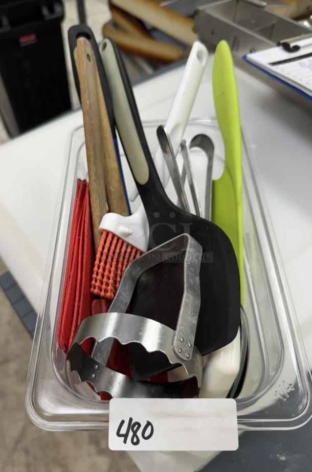 Assorted kitchen items in clear container, includes spatula, pastry brush, and metal cutter. Item labeled "480."
