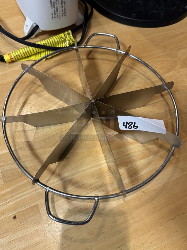 Metal pie cutter with handles, seven slices, excellent condition, tag labeled "486," on a wooden surface.
