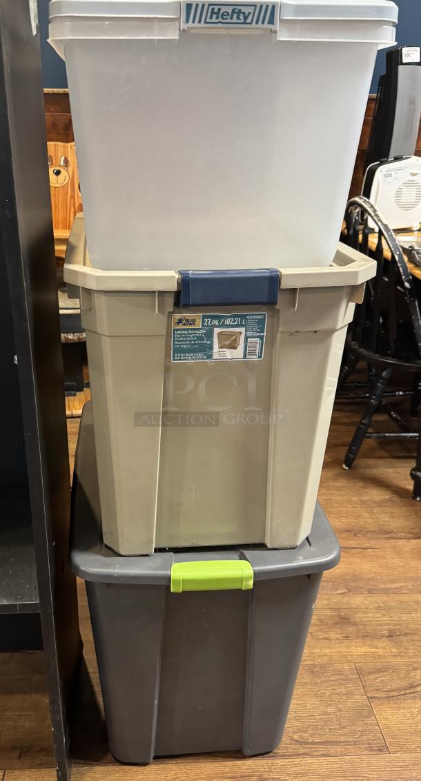 Three large plastic storage totes, mixed colors, stackable. Labels indicate "Hefty" and "Blue Hawk, 27 Gal/102.2 L". Used condition.