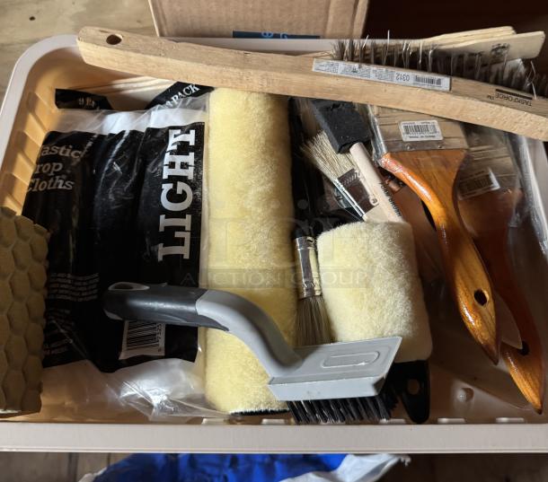 Assorted painting supplies in a bin, including new brushes, rollers, and drop cloths. Features wooden and plastic handles.