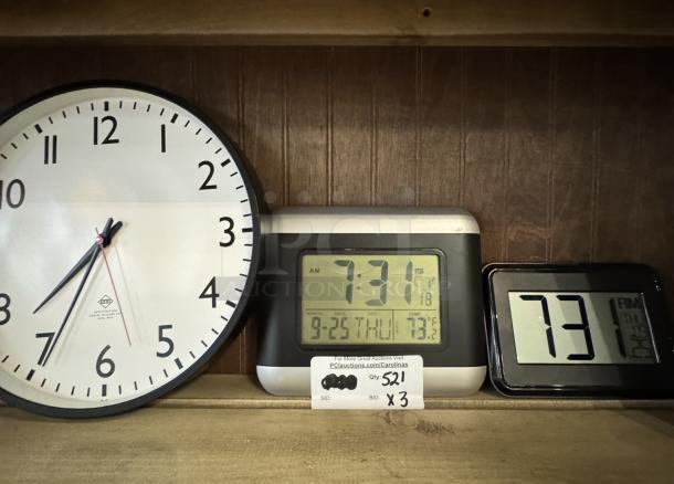 Assorted clocks: analog wall clock and two digital clocks, displaying time and temperature, on a wooden shelf.
