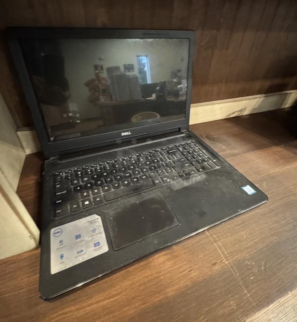 Dell Inspiron 15 3000 Series laptop, black, visible wear, open on a wooden surface. Intel and Windows stickers on palm rest.
