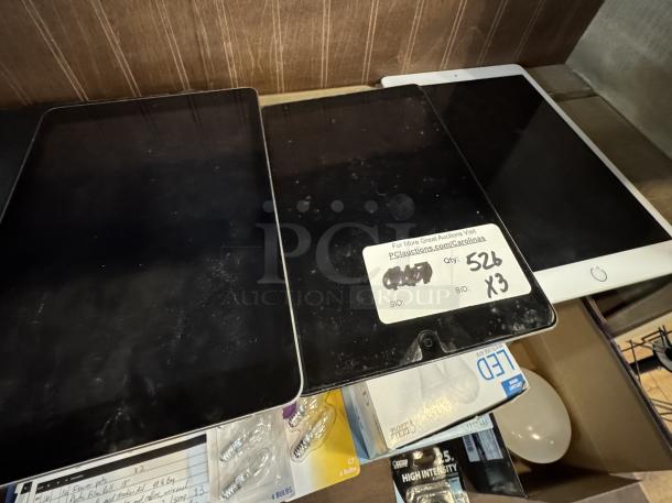 Three new Apple iPad Minis on display for auction, one with a label showing quantity 526 and bid x3, all in excellent condition.