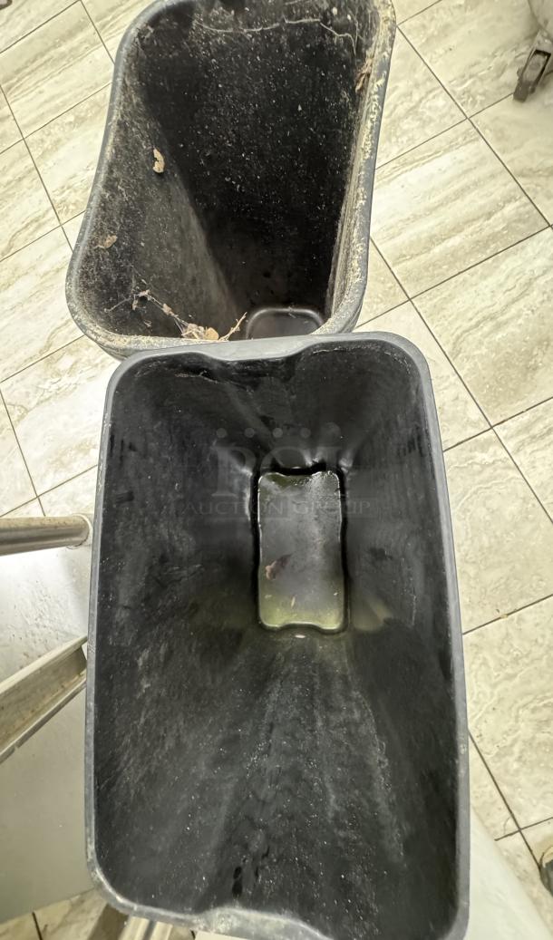 Two black rectangular trash cans, visibly worn and dusty, standing on a tiled floor.