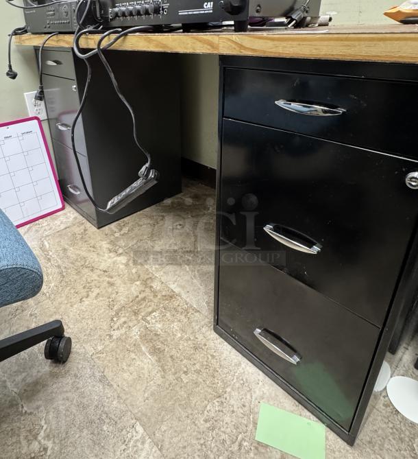 Wooden desk with two black metal filing cabinets, three drawers each, chrome handles, good condition, on tiled floor.