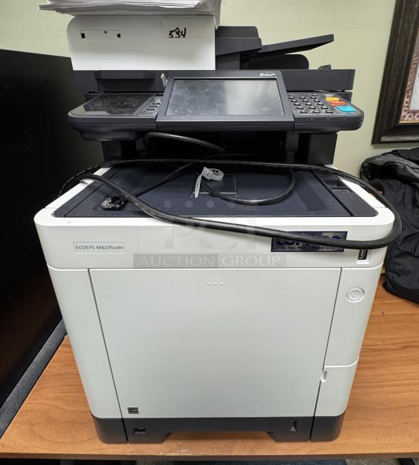 Ecosys M6235 printer with assorted paper, touchscreen, and control panel; shows model label, in used condition.