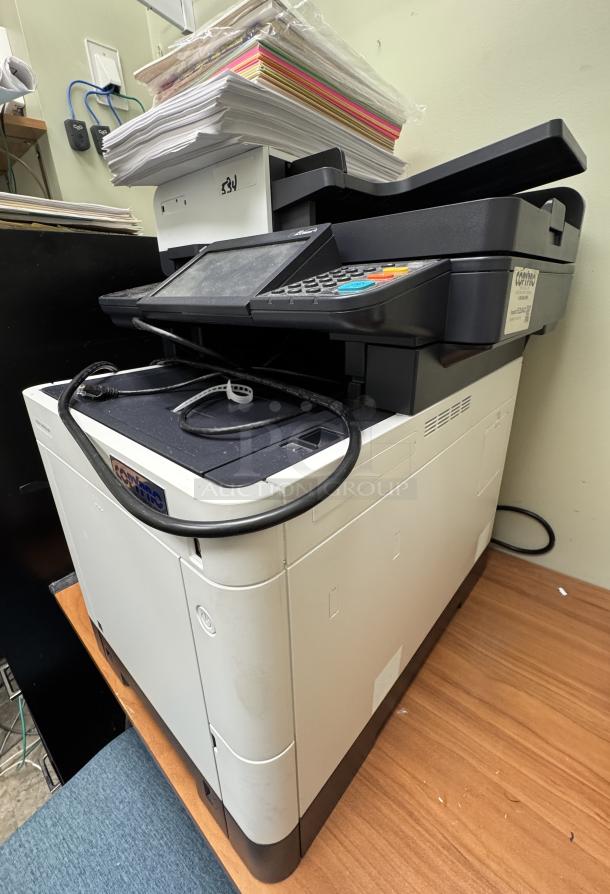 Ecosys M6235 printer in used condition with assorted paper on top, featuring control panel and visible wiring.