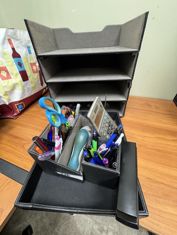Desk organizer tray with assorted pens, scissors, calculator, and office items. Four-tier shelf in background. Good condition.