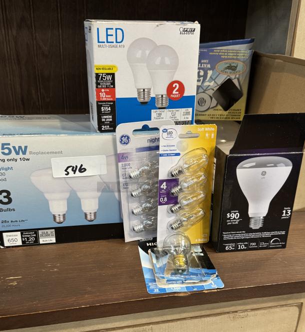 Assorted new light bulbs, including GE and Feit Electric brands, various wattages, and types, in original packaging.