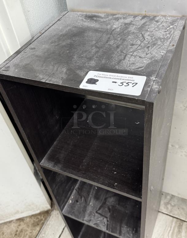 Black bookcase with 3 shelves, shows wear and dust. Auction label with bidding info on top. Condition suggests used item.