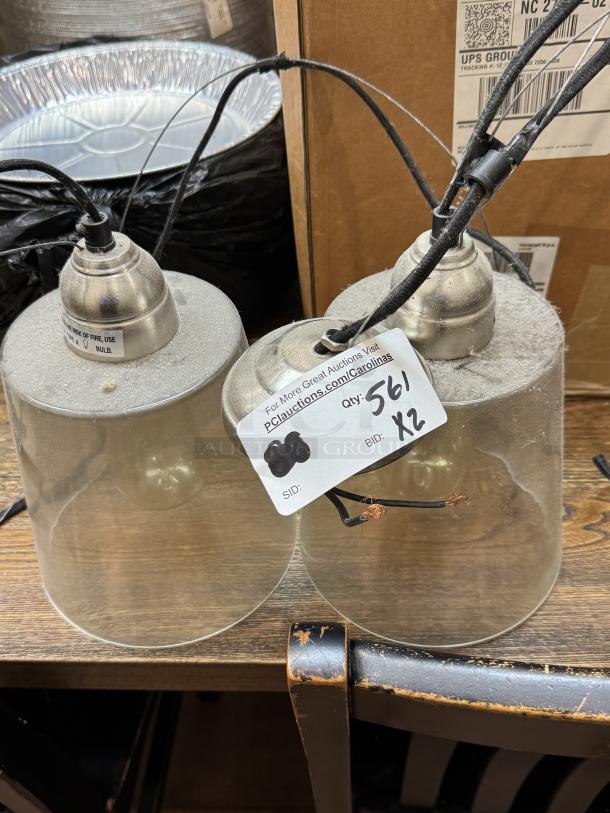 Two hanging pendant lights with brushed metal fittings and transparent glass shades, visible wires, auction tag displays "Qty: 2, BID: X2."